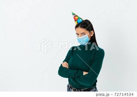 Sad young woman wearing a medical mask and a festive hat 72714534