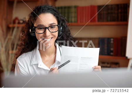 Woman in glasses sitting at desk, having videocall on laptop 72715542