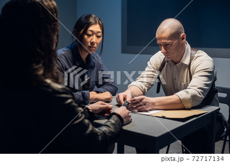 Two police officers a man and a woman are questioning the alleged offender at the police station Two police officers a man and a woman are questioning the alleged offender at the police station 72717134