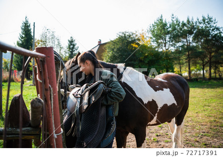 After a ride, the jockey unsaddles the horse next to the fence at the ranch After a ride, the jockey unsaddles the horse next to the fence at the ranch 72717391