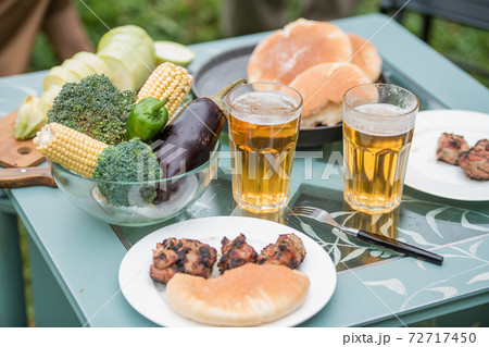 Close-up of a picnic table in the garden for two people. Food, grilled meat, grilled vegetables, beer. 72717450