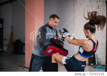 A young strong kickboxer girl kicks her sparring partner with a boxing paw in a personal training session 72722110