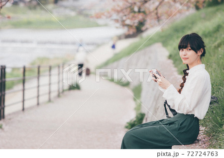 桜の背景とカメラを持っている白いシャツの女性 72724763