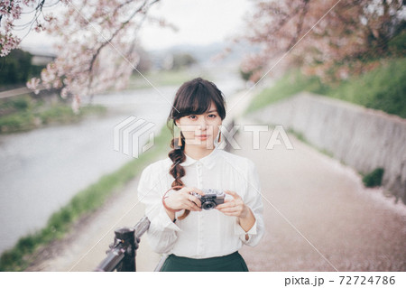桜の背景とカメラを持っている白いシャツの女性 72724786