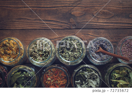 Jars of dry medicinal herbs - calendula, melissa, wild marjoram,  lavender, heather, coneflowers, raspberry and currant leaves, linden tree flowers on wooden table. Top view. Alternative medicine. 72735672