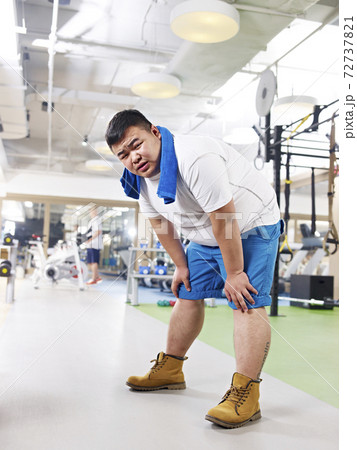 exhausted overweight young asian man in fitness center. exhausted overweight young asian man in fitness center. 72737821