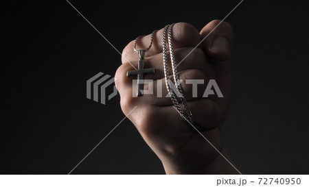 Cross or crucifix pendant and necklace in man hand on black color background in studio which represent praying for god or jesus and thank gods for giving peaceful and faithful to people. silver cross. Cross or crucifix pendant and necklace in man hand on black color background in studio which represent praying for god or jesus and thank gods for giving peaceful and faithful to people. silver cross. 72740950