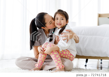 Asian mother kissing her daughter in bright bedroom at home. Asian mother kissing her daughter in bright bedroom at home. 72741718