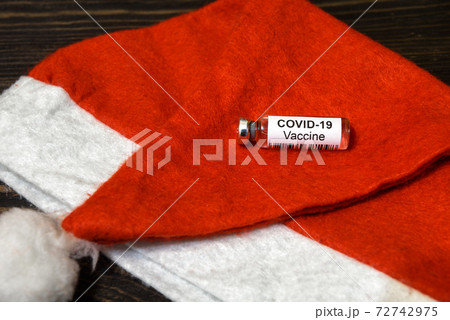 COVID-19 coronavirus vaccine bottle on red Santa hat for Christmas holiday celebration 72742975