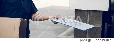 Young asian man smiling while delivering a cardboard box to the woman holding document to signing signature. 72749407