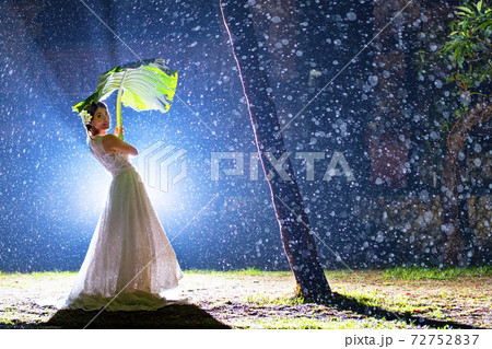 雨の中で葉っぱの傘を持つウェディングドレス姿の女性の写真素材