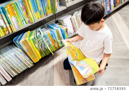 Asian little child sit on the floor,reading a cartoon from a fable book,happy kid boy enjoy in school library,excited kindergarten student looking at picture and color from fable book in a bookstore 72758393