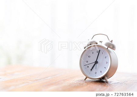 窓辺の机の上に置かれた朝日に照らされる目覚まし時計 72763564
