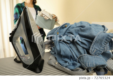 Iron on ironing board and woman with basket of laundry Iron on ironing board and woman with basket of laundry 72765324