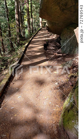 木漏れ日のさす登山道を歩くと前方に大きな岩が見えてきた・ファンタジー世界の実写化・山賊が出そうな様子 72769543