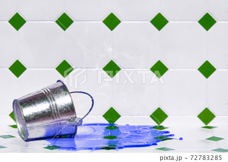 A colored liquid flows out of a metal bucket on a white tiles. A colored liquid flows out of a metal bucket on a white tiles. 72783285