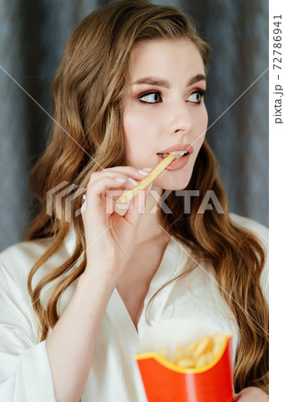 beautiful young woman with long hair and makeup eating French fries. beautiful young woman with long hair and makeup eating French fries. 72786941