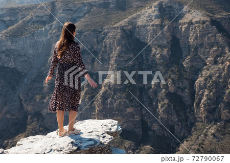 Long haired brunette stands on dangerous rocky cliff edge 72790067