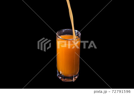 Freshly squeezed fruit juice is poured into a glass. Peach, orange or carrot on an isolated black background. 72791596