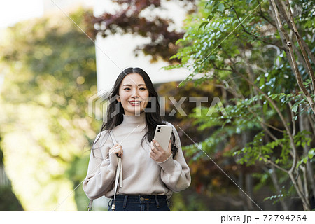 スマホを持って歩く若い女性 72794264