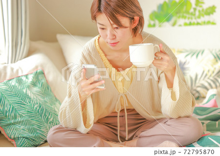 コーヒーカップを持ち座ってスマホを見る女性 コーヒーカップを持ち座ってスマホを見る女性 72795870