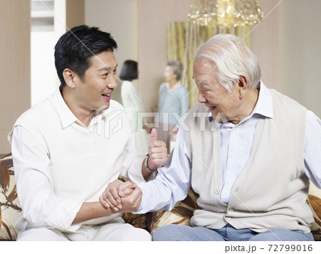 asian senior father and adult son sitting on couch chatting 72799016