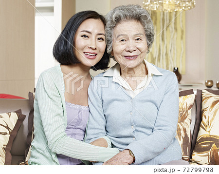 asian mother and adult daughter sitting on couch smiling 72799798
