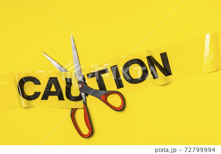 Studio shot of scissors cutting caution tape on yellow background Studio shot of scissors cutting caution tape on yellow background 72799994