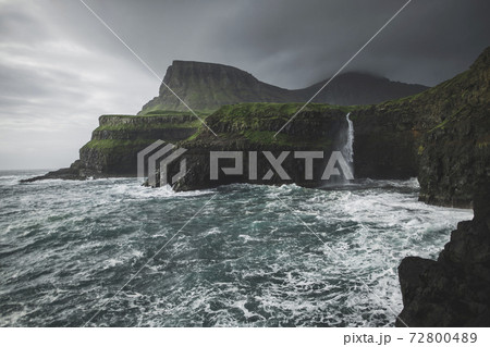 Denmark, Faroe Islands, Gasadalur Village, M·Lafossur Waterfall, Coastline with Mulafossur Waterfall falling into Atlantic Ocean in stormy day Denmark, Faroe Islands, Gasadalur Village, M·Lafossur Waterfall, Coastline with Mulafossur Waterfall falling into Atlantic Ocean in stormy day 72800489