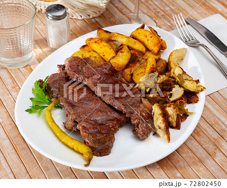 Delicious beef steak with baked potatoes and artichokes Delicious beef steak with baked potatoes and artichokes 72802450
