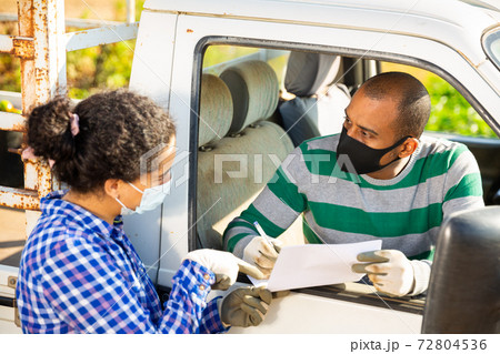 Farmer couple in protective masks discussing papers near car 72804536