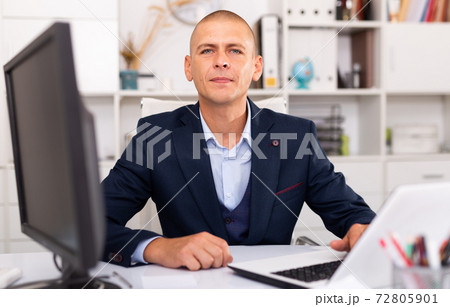 Positive businessman working with laptop and documents Positive businessman working with laptop and documents 72805901