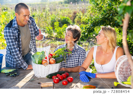 Family in garden talking after harvesting vegetables 72808454