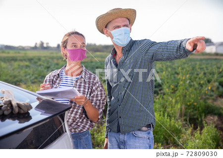 Hired worker in protective mask signs job application from farm owner next to car Hired worker in protective mask signs job application from farm owner next to car 72809030
