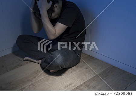 暗い部屋で床に座っている男性 72809063