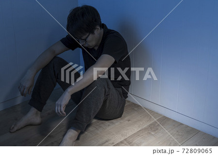 暗い部屋で床に座っている男性 72809065