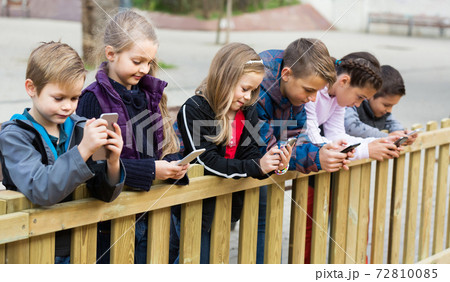 Outdoor portrait of girls and boys playing with phones 72810085