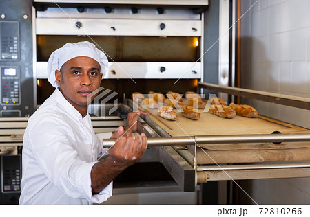 Male bakery worker pulls bread pan out of oven 72810266