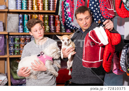 Father and son choose clothes for dogs in pet store 72810375