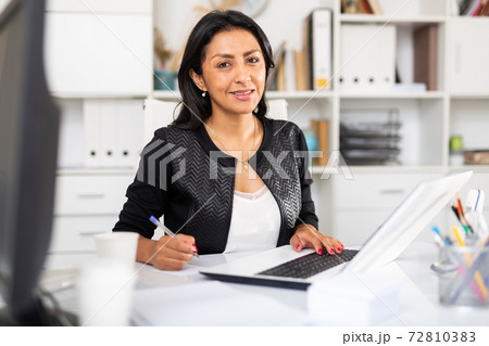 Smiling female office employee working with laptop and documents 72810383