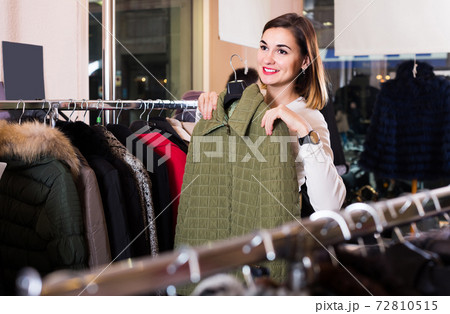 woman choosing green quilted jacket in women’s cloths store 72810515