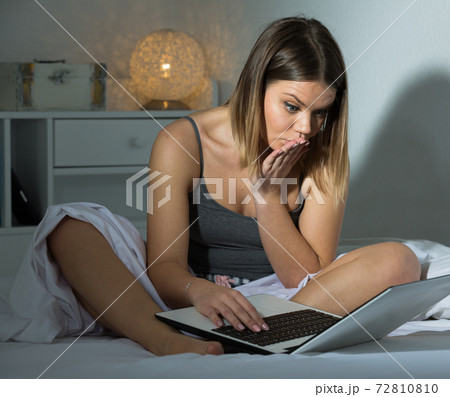 Sexy worried female siting with laptop on bed, holding arm near mouth Sexy worried female siting with laptop on bed, holding arm near mouth 72810810