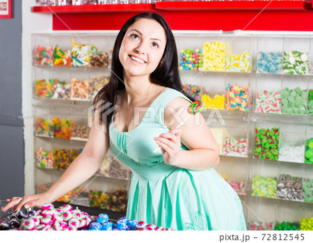 Smiling girl sucking lollypop in store Smiling girl sucking lollypop in store 72812545
