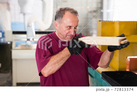 Elderly worker checks metal detail on a wooden sample Elderly worker checks metal detail on a wooden sample 72813374