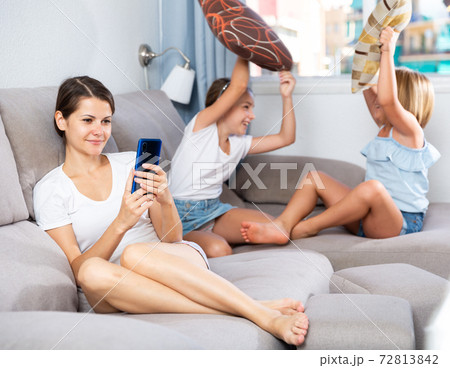 Woman using phone while daughters pillow fighting Woman using phone while daughters pillow fighting 72813842