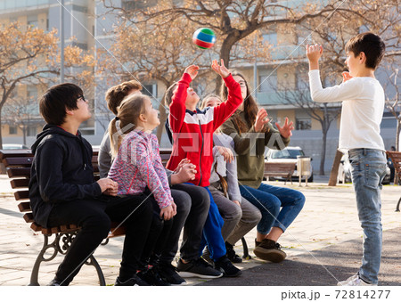 Group of cheerful children relaxing on bench on playground, playing with ball 72814277