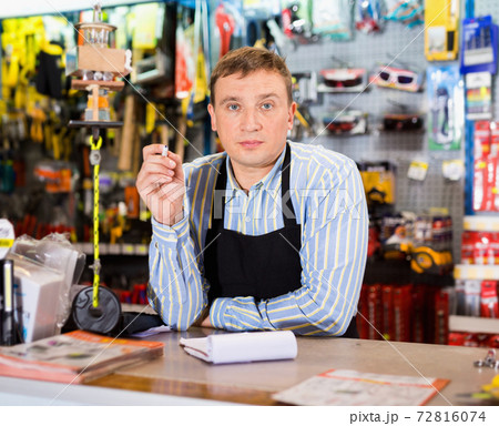Man seller wearing uniform having tools in hands in store Man seller wearing uniform having tools in hands in store 72816074
