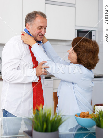 Mature woman adjusting tie to man at kitchen table at home interior Mature woman adjusting tie to man at kitchen table at home interior 72816245