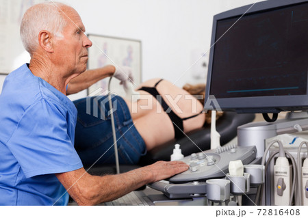 Elderly man sonographer using ultrasonography machine checking female patient in hospital diagnostic room 72816408