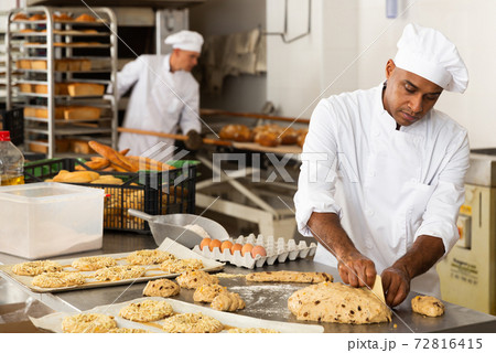 male baker in white uniform rolling out dough in kitchen 72816415